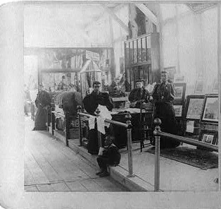 Interior of the Negro Building at the 1895 Cotton States Exposition: exhibit cases, framed pictures, and visitors in the hall.